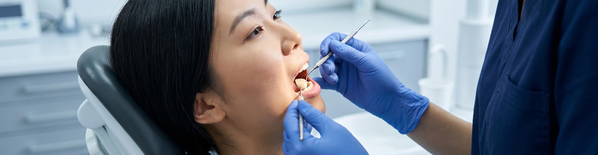 Gloved hands using dental tools in female's mouth.